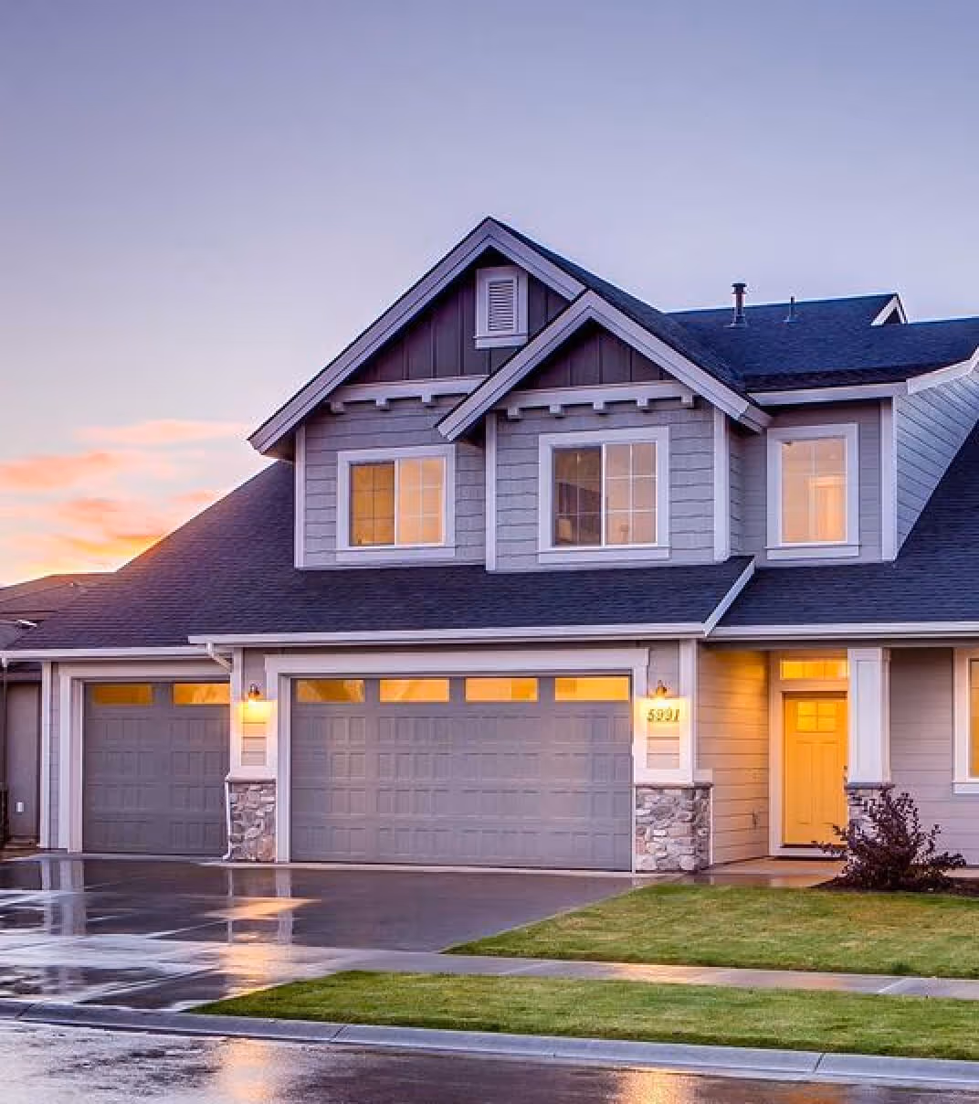 Modern two-story suburban home with gray siding, large garage, and well-kept lawn at sunset.