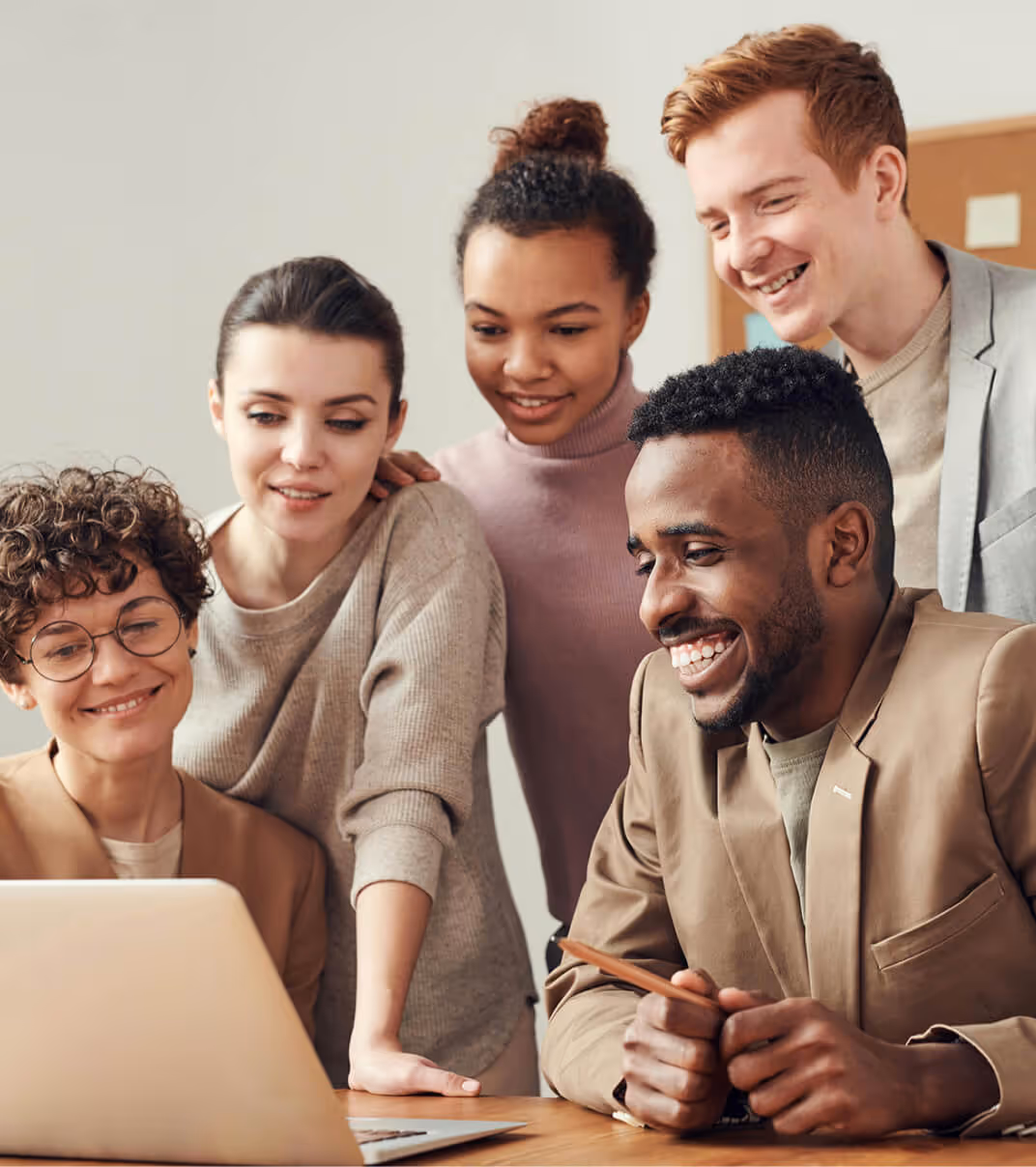 Group of professionals collaborating and smiling while reviewing a project on a laptop in a modern office setting.