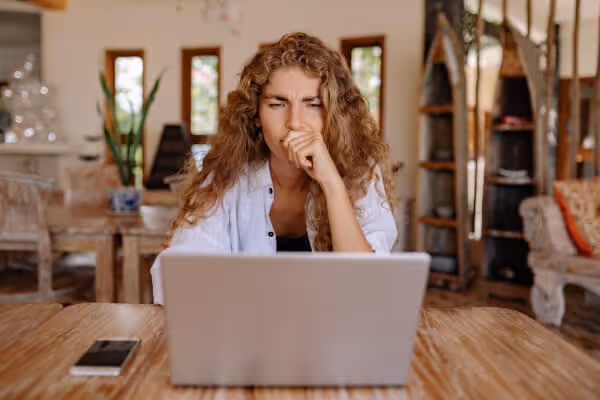 Professional working from home looking frustrated while reading emails on a laptop.